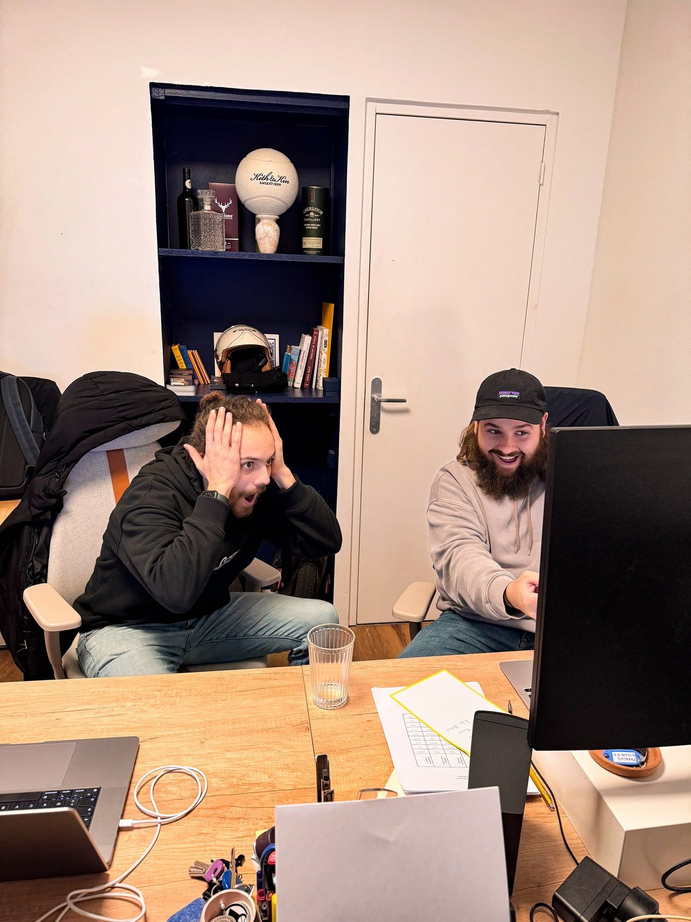 Léo, les mains sur la tête, et Seb, hilare, devant les écrans du bureau à l'heure du dispatch