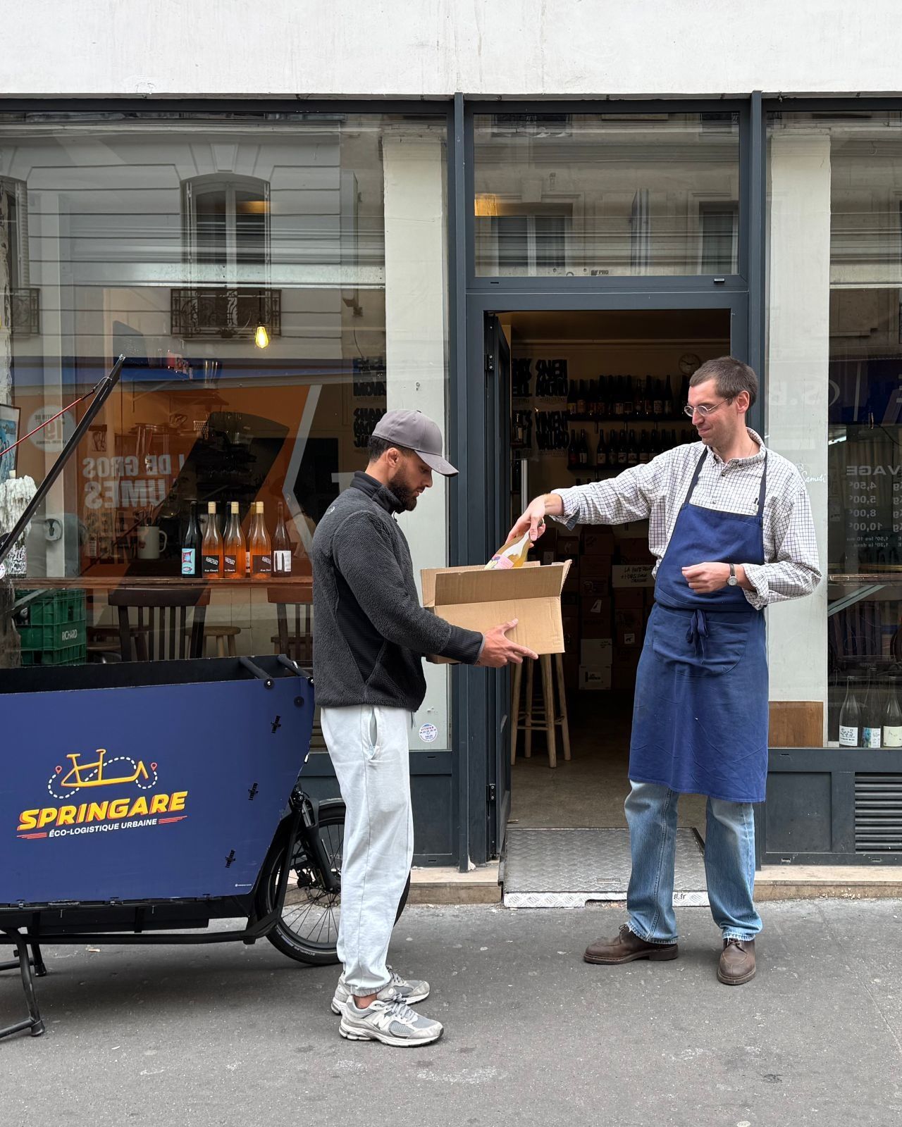 Un coursier Springare reçoit un carton de bouteilles des mains d'un caviste, devant sa boutique parisienne