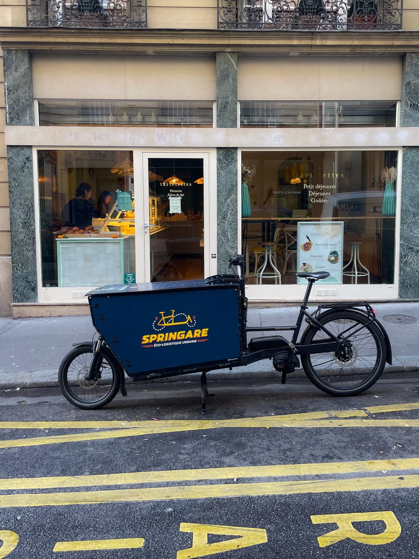 Un vélo cargo Springare garé le long du trottoir, devant la vitrine de la pâtisserie Tartelettes