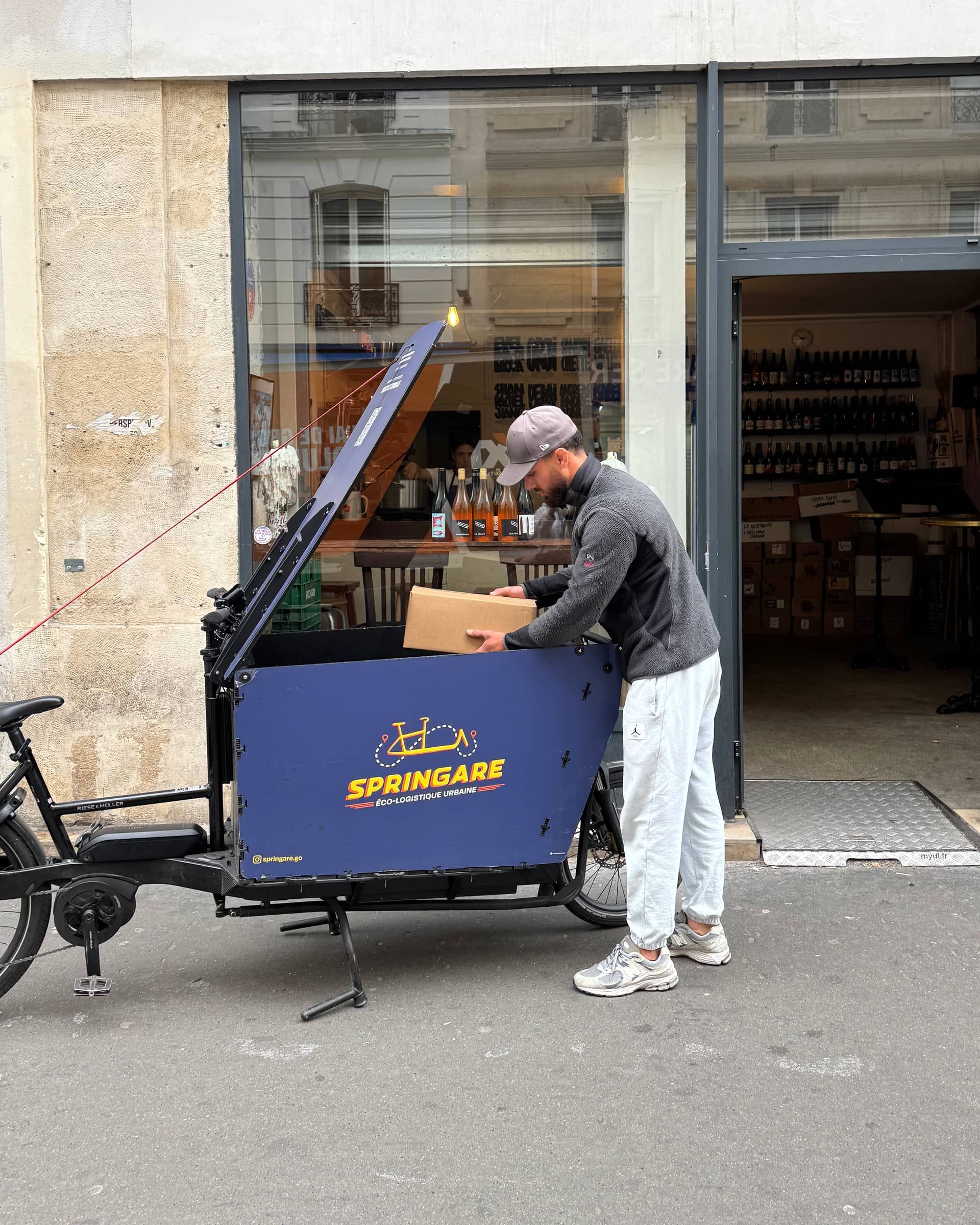 Un coursier Springare sort un carton du caisson de son vélo cargo devant un caviste parisien